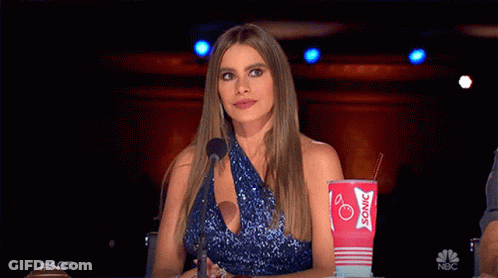 A Woman In A Blue Dress Is Sitting In Front Of A Microphone Holding A Sonic Cup GIF