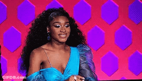 A Woman In A Blue Dress Is Sitting In Front Of A Pink And Purple Wall . GIF