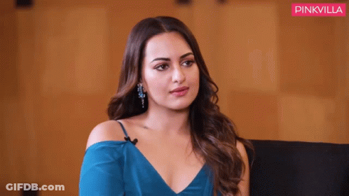 A Woman In A Blue Dress Is Sitting In Front Of A Pink Villa Banner GIF