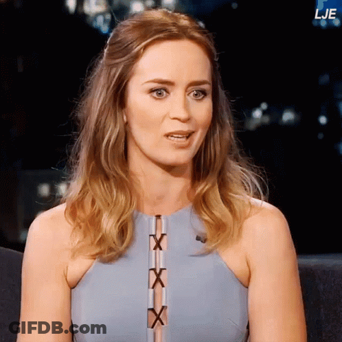 A Woman In A Blue Dress Is Sitting In Front Of A Sign That Says Lje GIF