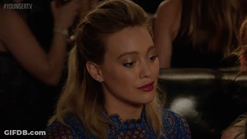 A Woman In A Blue Dress Is Sitting On A Couch In A Crowd Of People . GIF