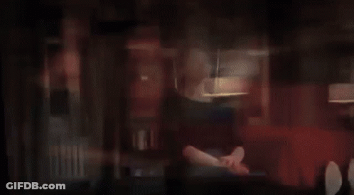 A Woman In A Blue Dress Is Sitting On A Couch In A Living Room With Headphones On . GIF