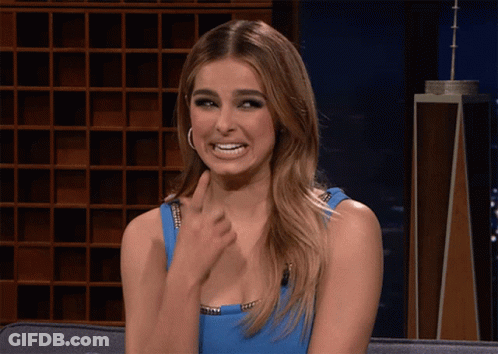 A Woman In A Blue Dress Is Sitting On A Couch Making A Funny Face GIF
