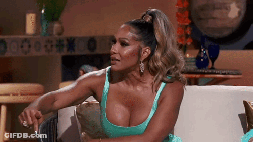 A Woman In A Blue Dress Is Sitting On A Couch With Her Hands On Her Knees . GIF