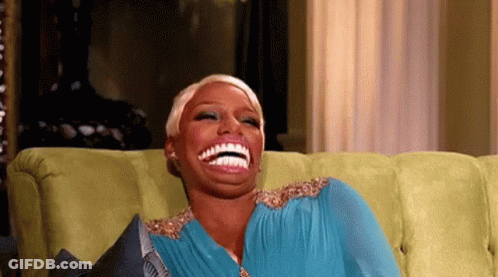 A Woman In A Blue Dress Is Sitting On A Green Couch And Laughing . GIF