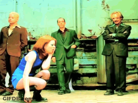 A Woman In A Blue Dress Is Squatting Down In Front Of Three Men In Suits GIF
