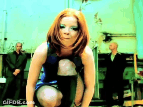 A Woman In A Blue Dress Is Squatting Down With A Man In A Suit Behind Her GIF