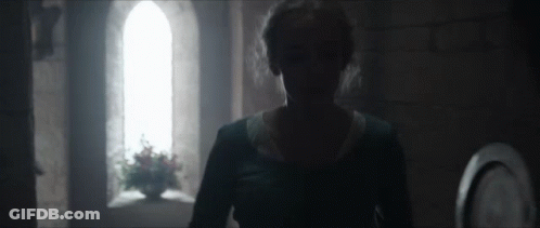 A Woman In A Blue Dress Is Standing In A Dark Room In Front Of A Window . GIF