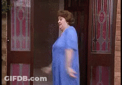 A Woman In A Blue Dress Is Standing In A Doorway GIF