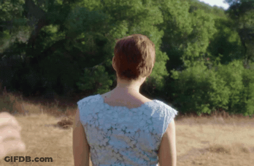 A Woman In A Blue Dress Is Standing In A Field With Trees In The Background GIF