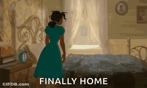 A Woman In A Blue Dress Is Standing In Front Of A Bed With The Words Finally Home Written Below Her GIF