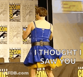 A Woman In A Blue Dress Is Standing In Front Of A Comic Con Sign . GIF
