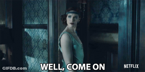 A Woman In A Blue Dress Is Standing In Front Of A Door And Says Well Come On GIF