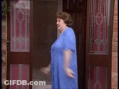 A Woman In A Blue Dress Is Standing In Front Of A Door GIF