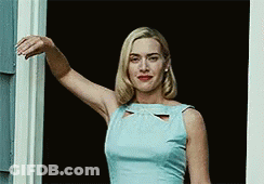 A Woman In A Blue Dress Is Standing In Front Of A Door . GIF