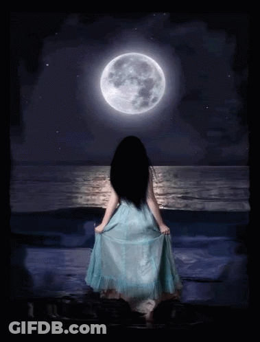A Woman In A Blue Dress Is Standing In Front Of A Full Moon Over The Ocean GIF