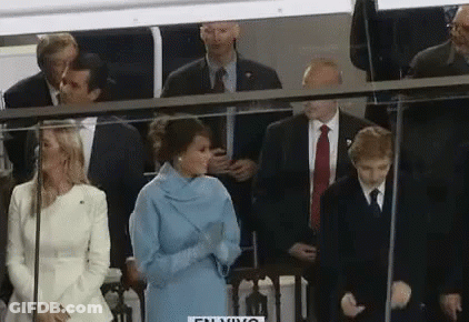 A Woman In A Blue Dress Is Standing In Front Of A Group Of People In Suits And Ties . GIF