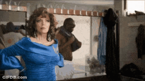 A Woman In A Blue Dress Is Standing In Front Of A Mirror Looking At Herself GIF