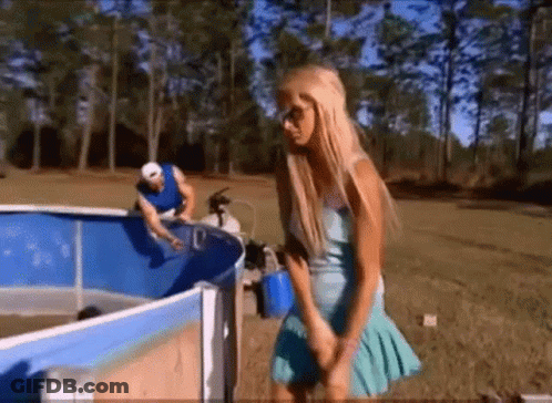 A Woman In A Blue Dress Is Standing In Front Of A Swimming Pool GIF