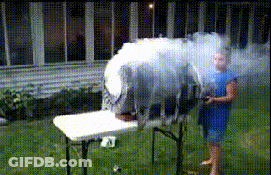 A Woman In A Blue Dress Is Standing In Front Of A Table With Smoke Coming Out Of It GIF