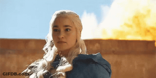A Woman In A Blue Dress Is Standing In Front Of A Wall With A Fire In The Background . GIF
