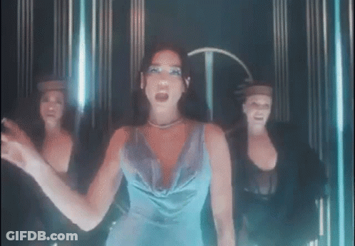 A Woman In A Blue Dress Is Standing In Front Of Three Dancers In A Dark Room . GIF