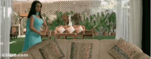 A Woman In A Blue Dress Is Standing Next To A Couch In A Living Room GIF