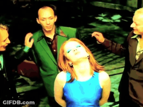 A Woman In A Blue Dress Is Surrounded By Men In Green Suits . GIF