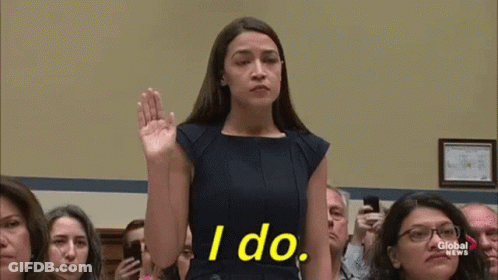 A Woman In A Blue Dress Is Taking A Oath In Front Of A Crowd Of People . GIF
