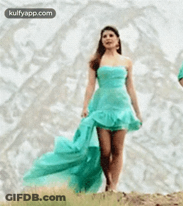 A Woman In A Blue Dress Is Walking Across A Hill . GIF