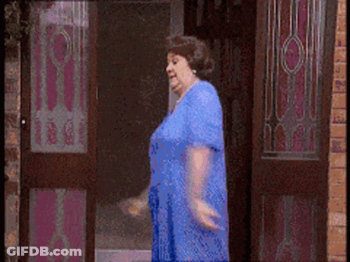 A Woman In A Blue Dress Is Walking Through A Door GIF