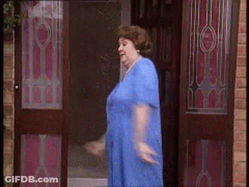 A Woman In A Blue Dress Is Walking Through A Doorway GIF