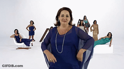 A Woman In A Blue Dress Stands In Front Of A Group Of Women In Different Dresses GIF