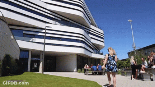 A Woman In A Blue Dress Stands In Front Of A Large Building GIF