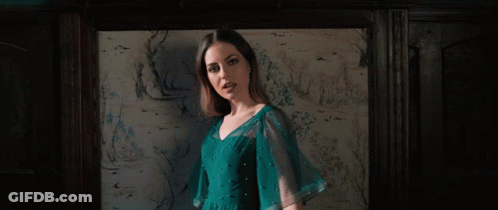 A Woman In A Blue Dress Stands In Front Of A Wall With Drawings On It GIF