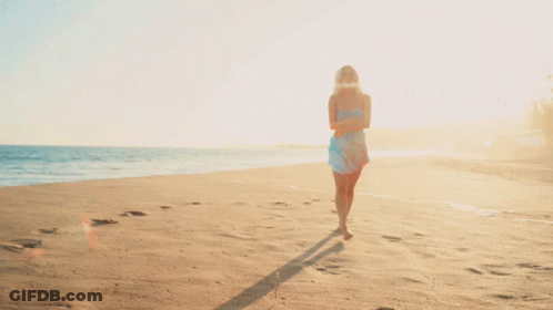 A Woman In A Blue Dress Walking On A Beach GIF