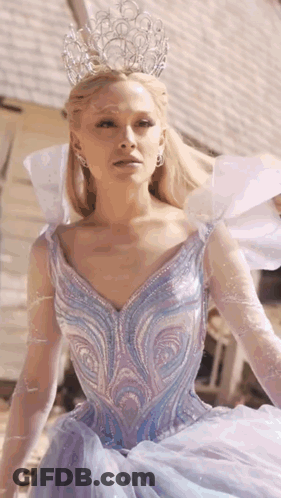 A Woman In A Blue Dress With A Crown On Her Head Is Standing In Front Of A Building . GIF