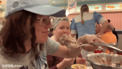 A Woman In A Blue Hat Is Being Served Food By Another Woman In A Diner GIF