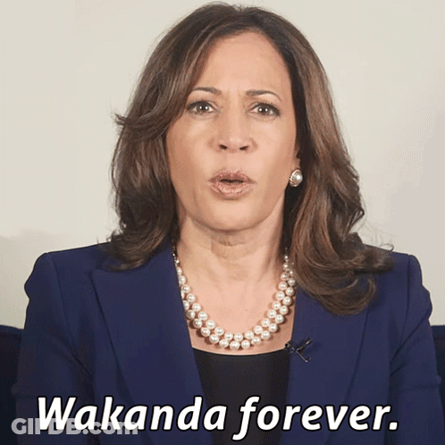 A Woman In A Blue Jacket And Pearl Necklace Says Wakanda Forever GIF