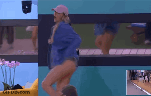 A Woman In A Blue Jacket And Pink Hat Is Dancing In Front Of A Window GIF