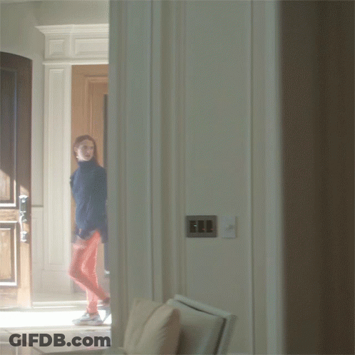 A Woman In A Blue Jacket And Red Pants Is Walking Through A Doorway GIF