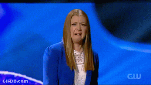 A Woman In A Blue Jacket And White Shirt Is Making A Funny Face On A Blue Background . GIF