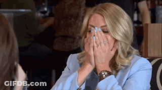 A Woman In A Blue Jacket Is Covering Her Face With Her Hands While Sitting At A Table . GIF
