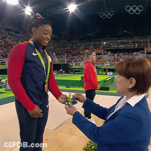 A Woman In A Blue Jacket Is Giving A Medal To Another Woman GIF