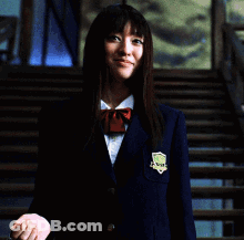 A Woman In A Blue Jacket Is Holding A Chain Around Her Neck And Smiling GIF