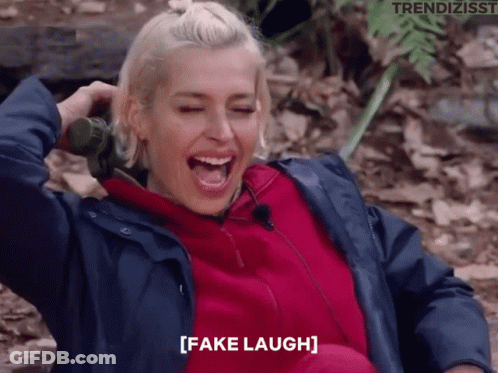 A Woman In A Blue Jacket Is Laughing With The Words Fake Laugh Written Below Her GIF