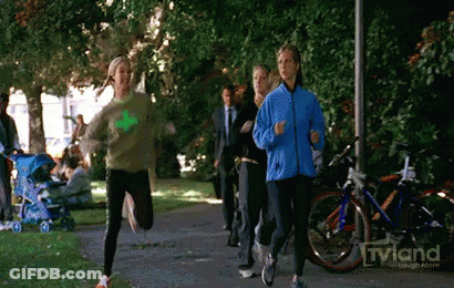 A Woman In A Blue Jacket Is Running In A Park With A Tvland Logo In The Background GIF