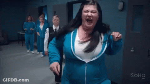 A Woman In A Blue Jacket Is Standing In A Hallway With A Group Of Women . GIF