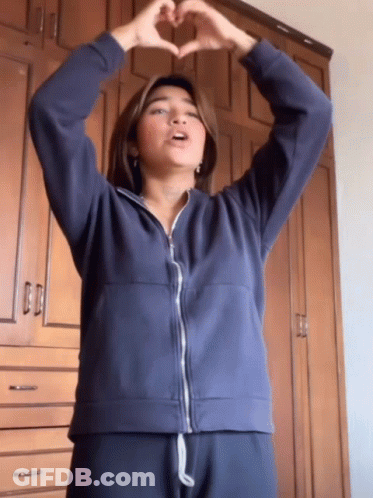 A Woman In A Blue Jacket Making A Heart With Her Hands GIF