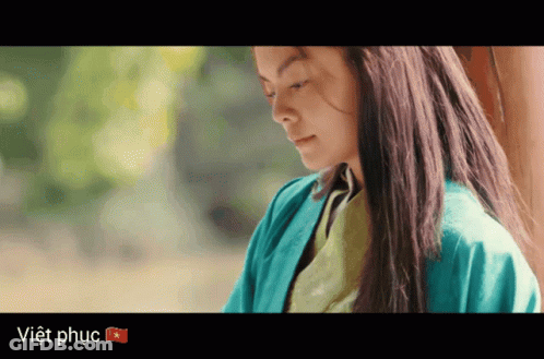 A Woman In A Blue Jacket Stands In Front Of A Sign That Says Viet Phuc GIF